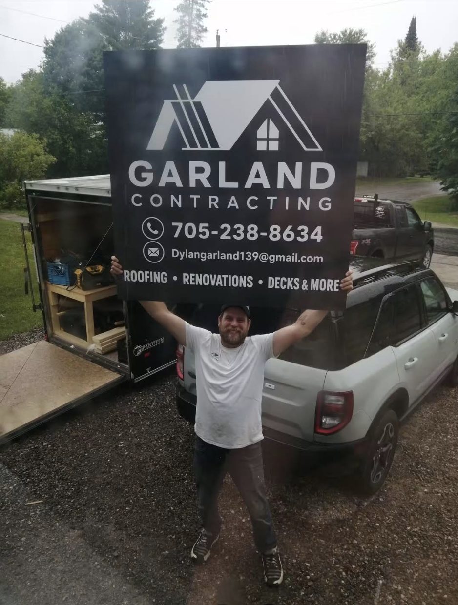 Dylan Garland holding up the Garland Contracting sign in front of a work trailer