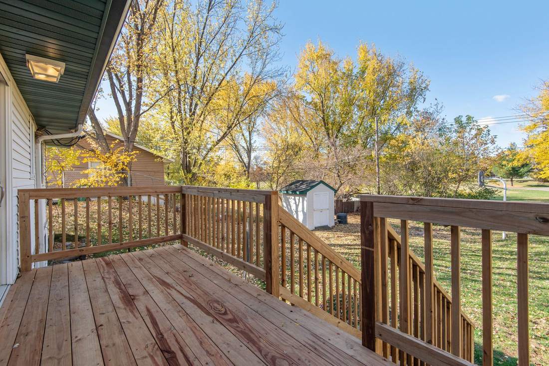 New wooden deck with railing and stairs beside a house, with autumn trees behind