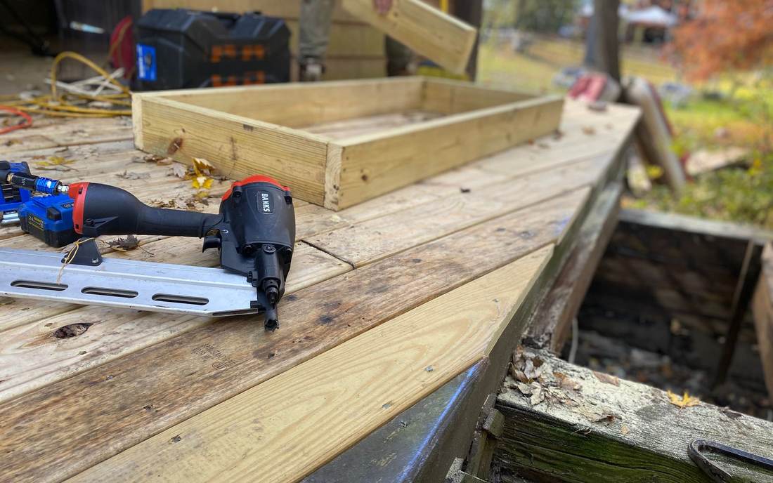 Framing nailer and new pressure-treated lumber on a deck being rebuilt beside rotted, weathered framing
