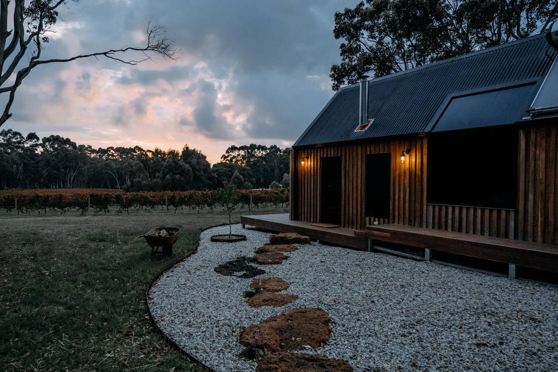 Dark vertical wood siding on a modern cabin at dusk, with a deck and lit windows